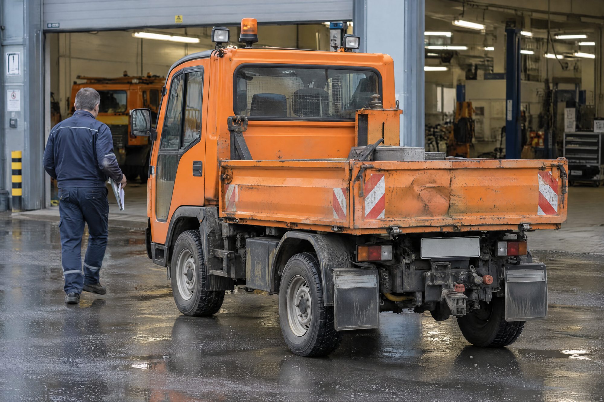 Kommunalfahrzeug vor dem offenen Werkstatttor, Mechaniker mit Klemmbrett